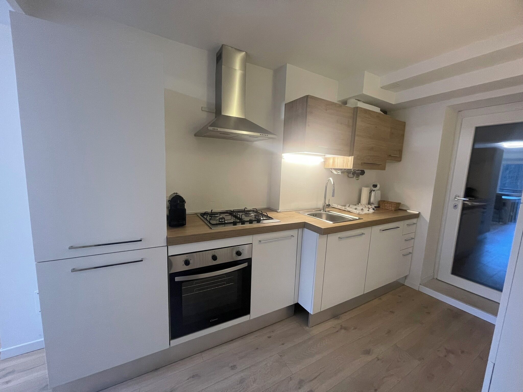 A modern kitchen with white cabinets, a stainless steel range hood, a built-in oven, and a wooden countertop.