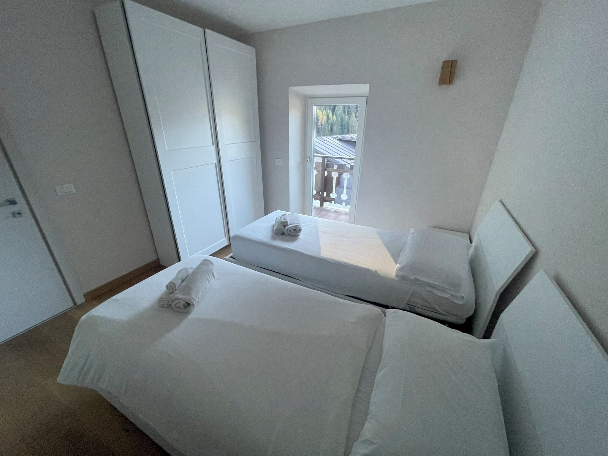 A bedroom with two beds, a wardrobe, and a window with a view of trees.