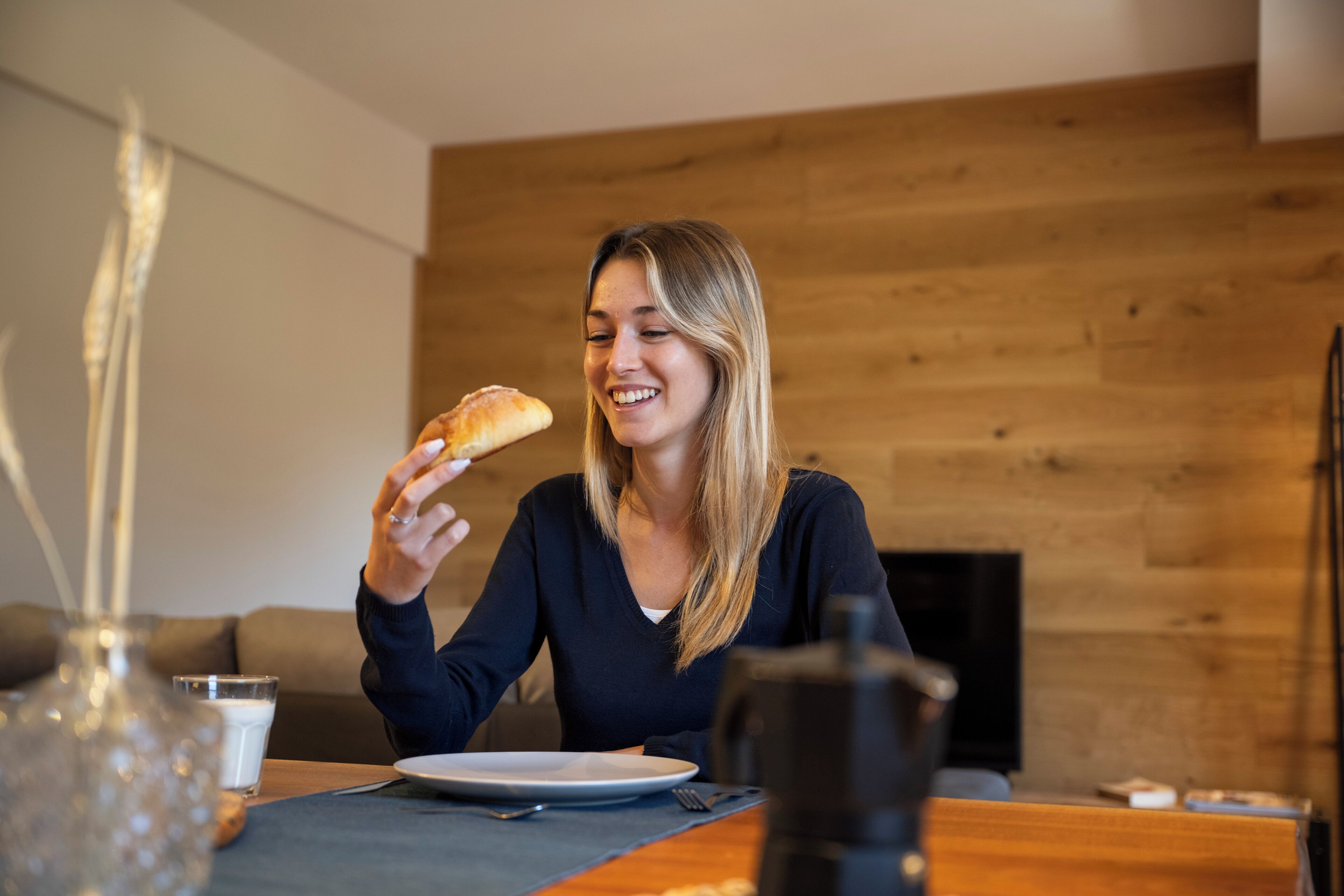 Une personne est assise à une table devant une assiette, un verre de lait et une machine à café.