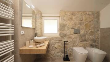 Ein modernes Badezimmer mit Steinwand, Waschtisch aus Holz, großem Spiegel, weißem Waschbecken, Toilette und Bidet.