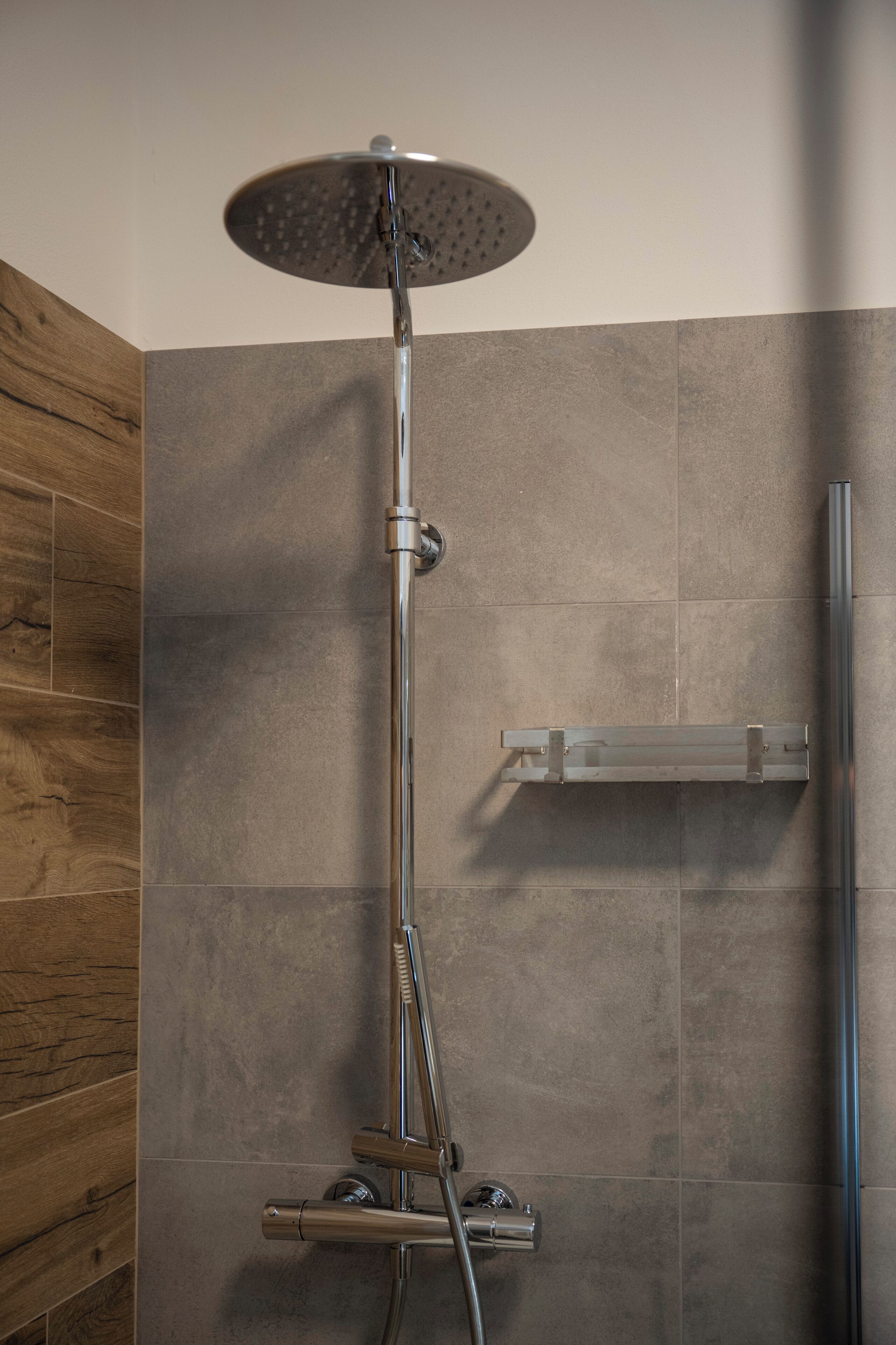 Una ducha moderna con cabezal de ducha de mano y panel de control empotrado.