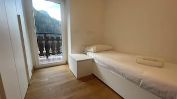 Une petite chambre avec un lit simple, un plancher en bois, un lit blanc et un balcon offrant une vue sur la montagne.