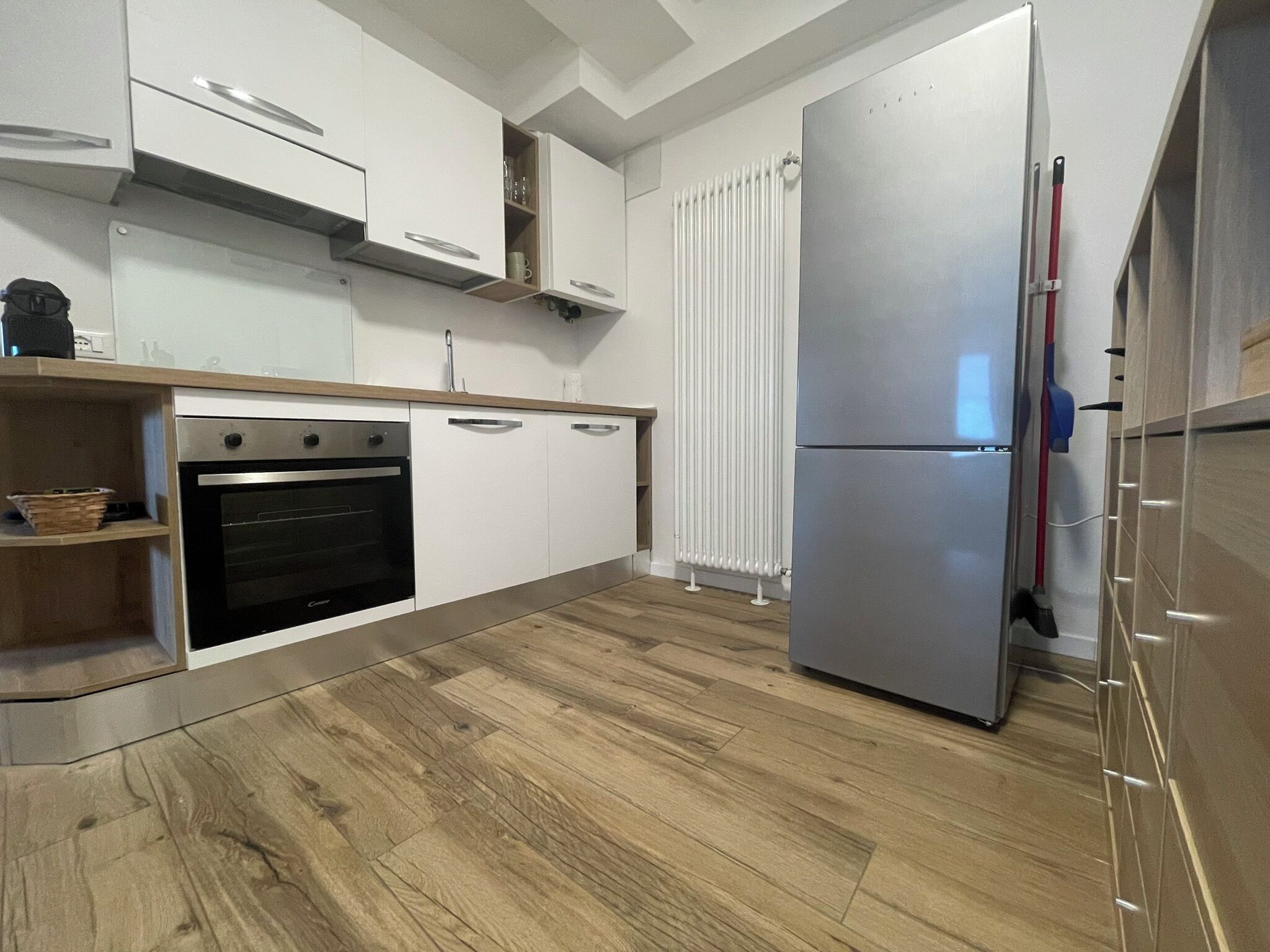 A modern kitchen with white cabinets, a built-in oven, a double-door refrigerator, and a wooden floor.