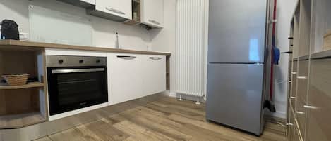 A modern kitchen with white cabinets, a built-in oven, a double-door refrigerator, and a wooden floor.