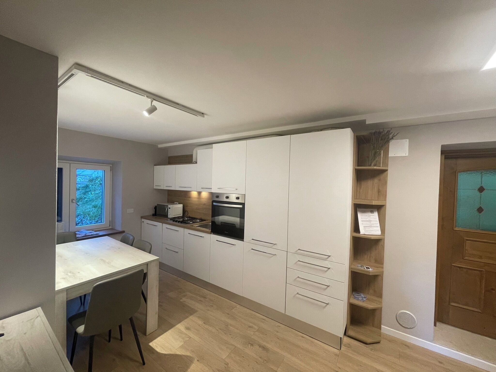 A compact kitchen with a built-in oven, microwave, and gas stove. There is a window providing natural light and a door with a decorative glass panel.