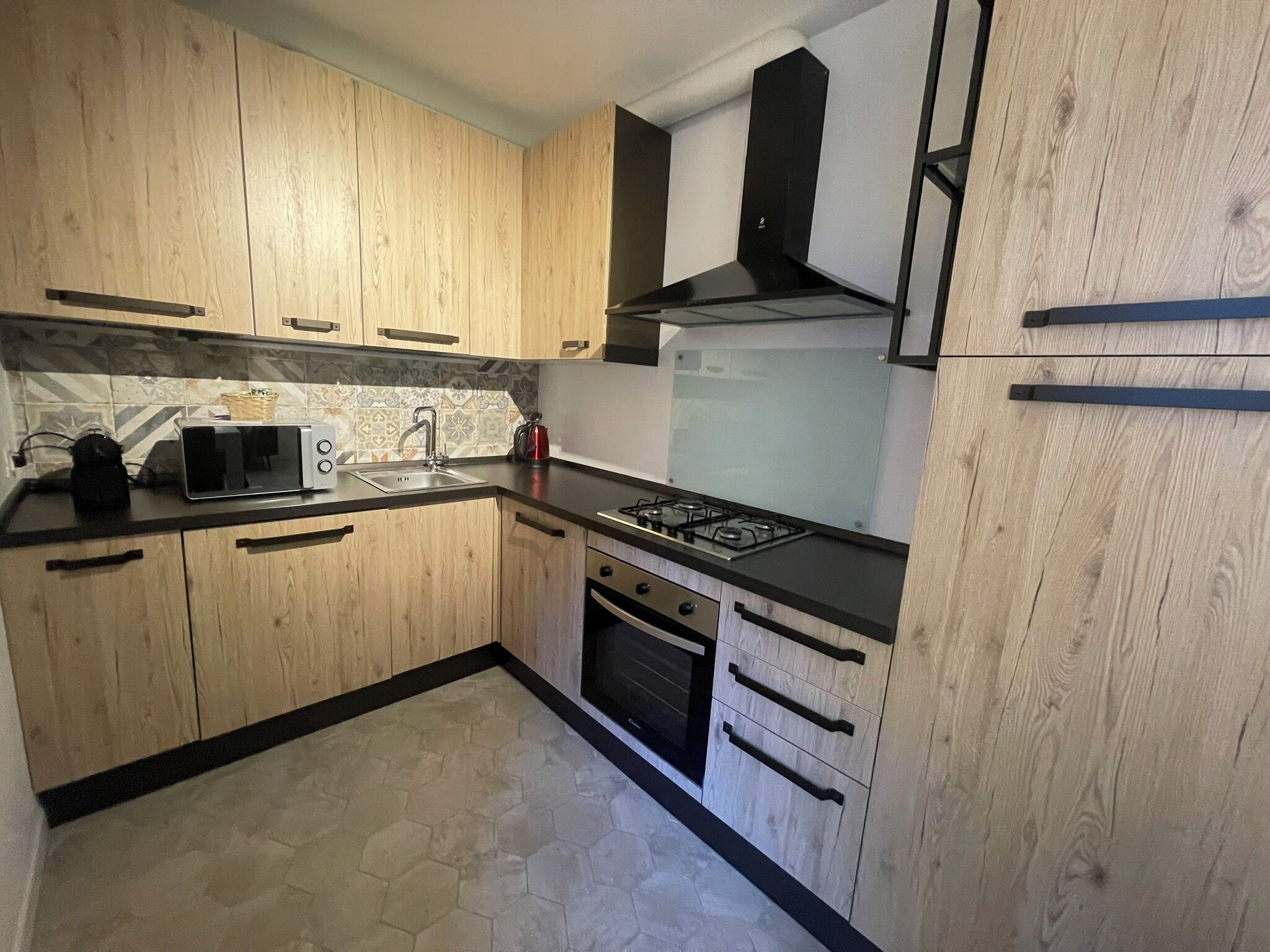 Una cocina moderna con armarios de madera, estufa a gas, microondas y un lavamanos.