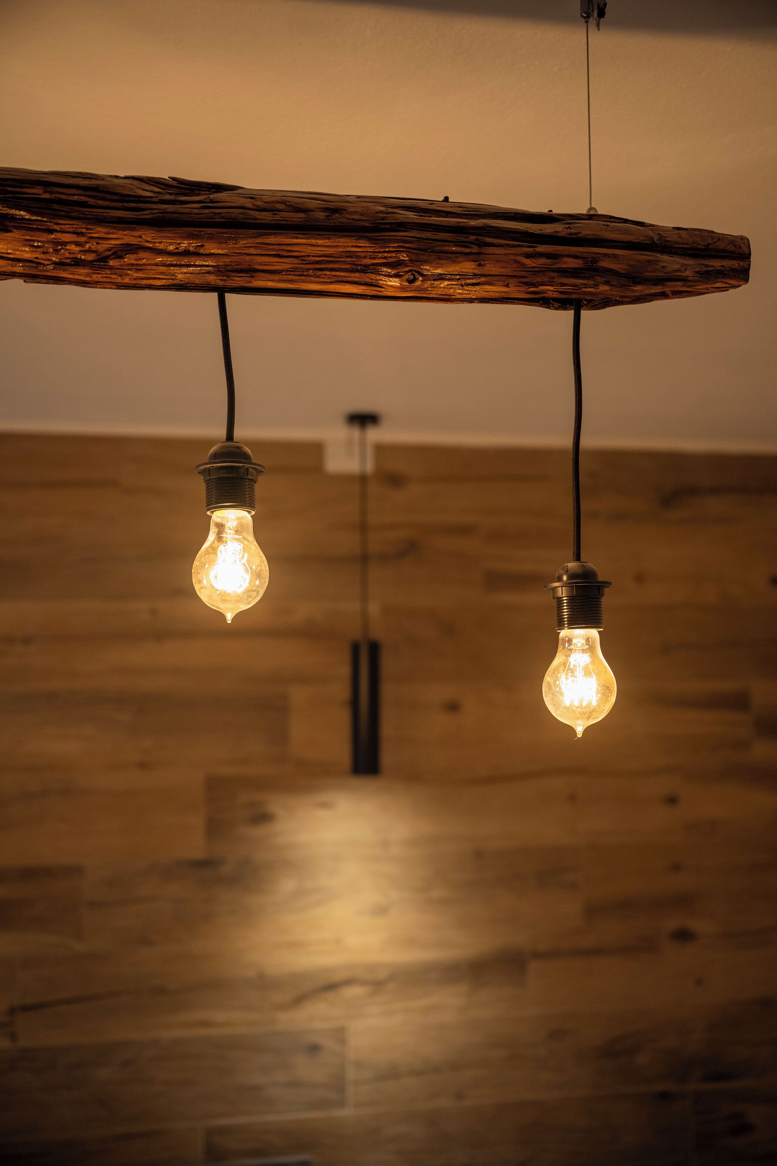 Two hanging light bulbs on a wooden beam.