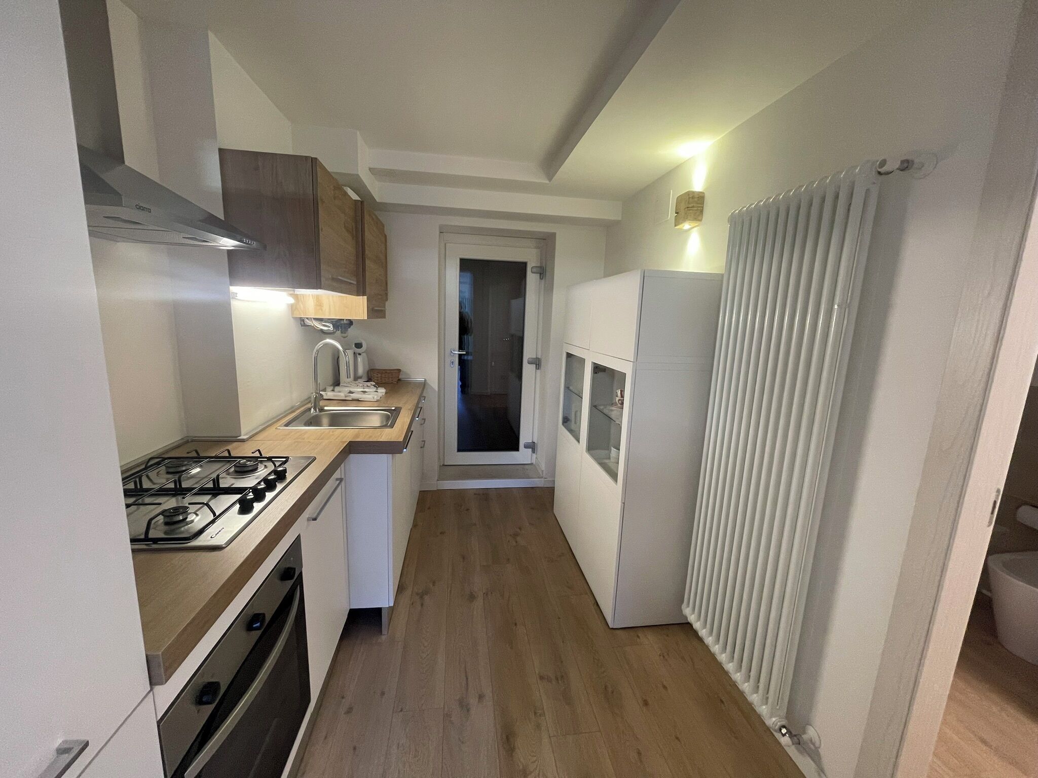 A narrow kitchen with a gas stove, sink, and white cabinets.