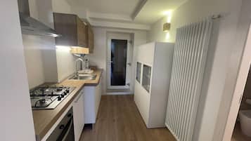 A narrow kitchen with a gas stove, sink, and white cabinets.