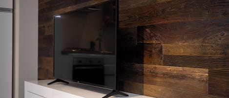 A flat-screen TV on a white stand against a wooden wall.