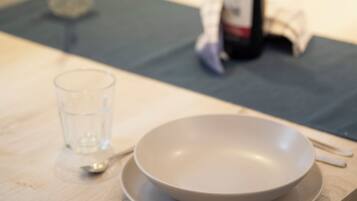 A dining table with a bowl, spoon, and glass, and a bottle in the background.