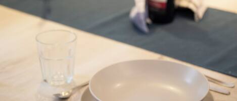 A dining table with a bowl, spoon, and glass, and a bottle in the background.