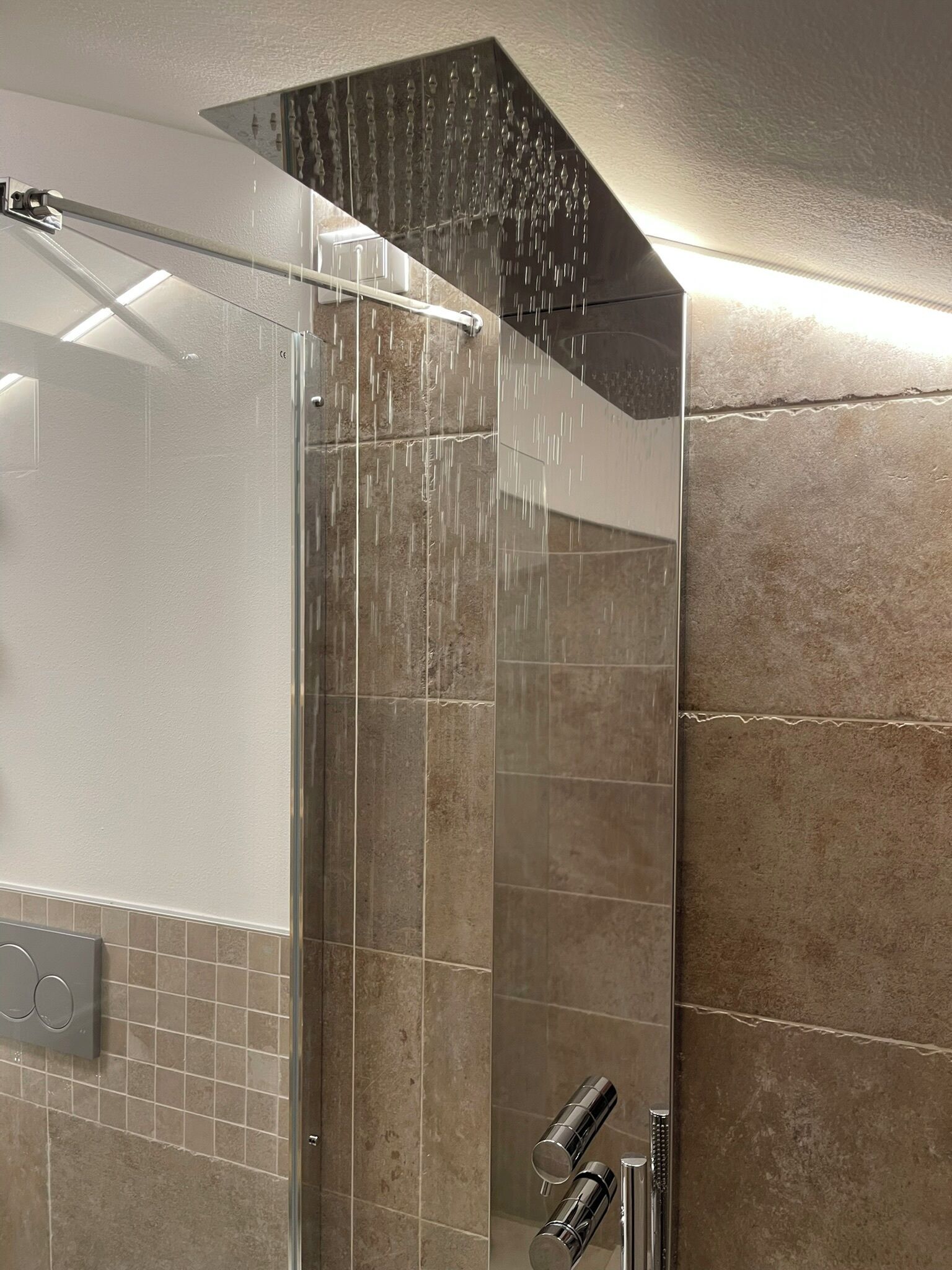 Une douche moderne dotée d’un pare-douche en verre et d’un pommeau de douche à effet pluie.
