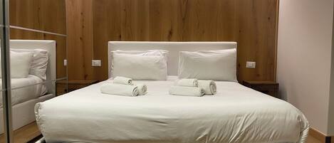 A modern bedroom with a large bed, two bedside tables, and a built-in wardrobe.