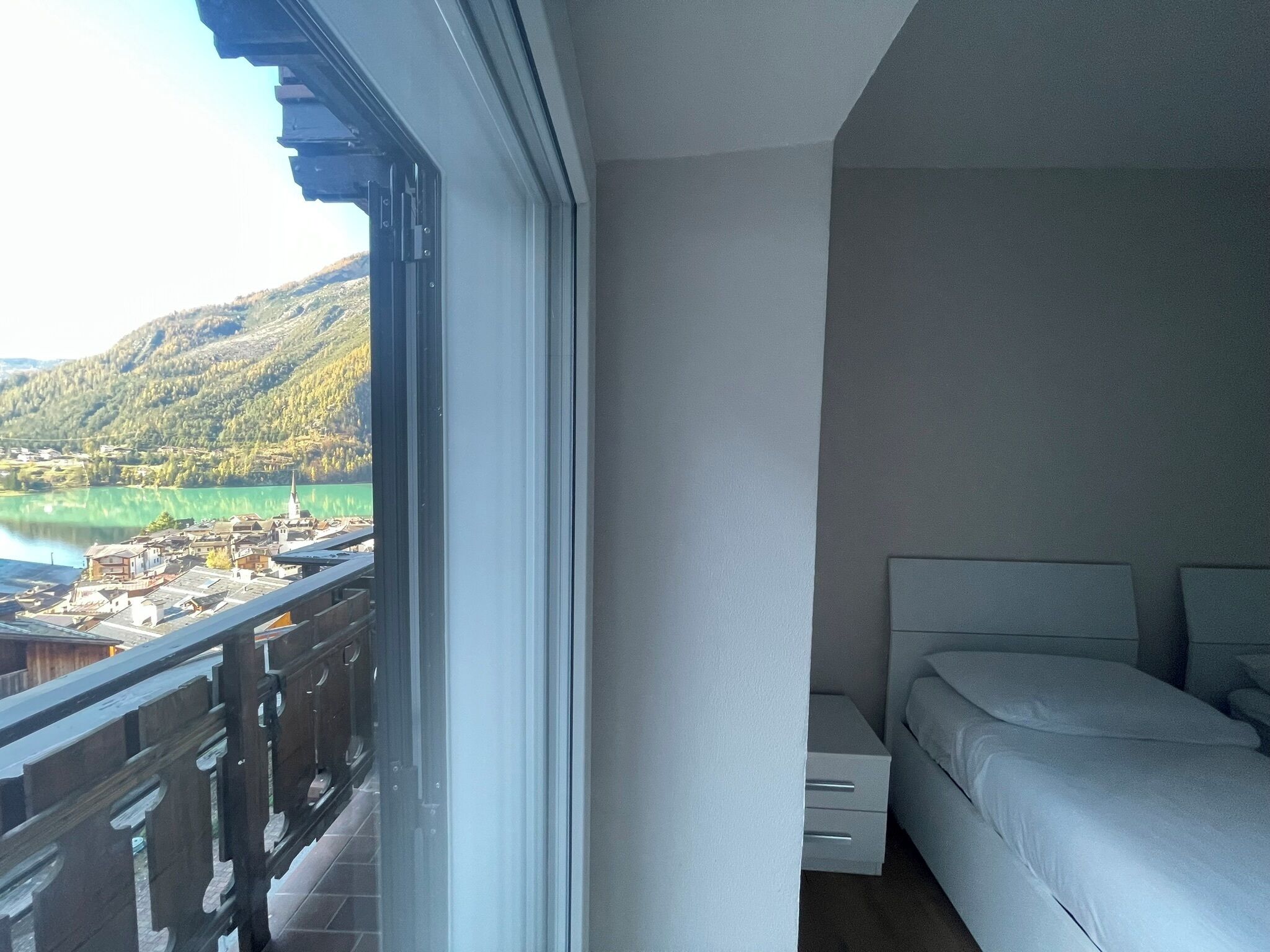 A bedroom with a balcony overlooking a lake and mountains.