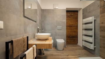 A modern bathroom with a large vessel sink, wooden vanity, a toilet, and a walk-in shower with a wooden wall.
