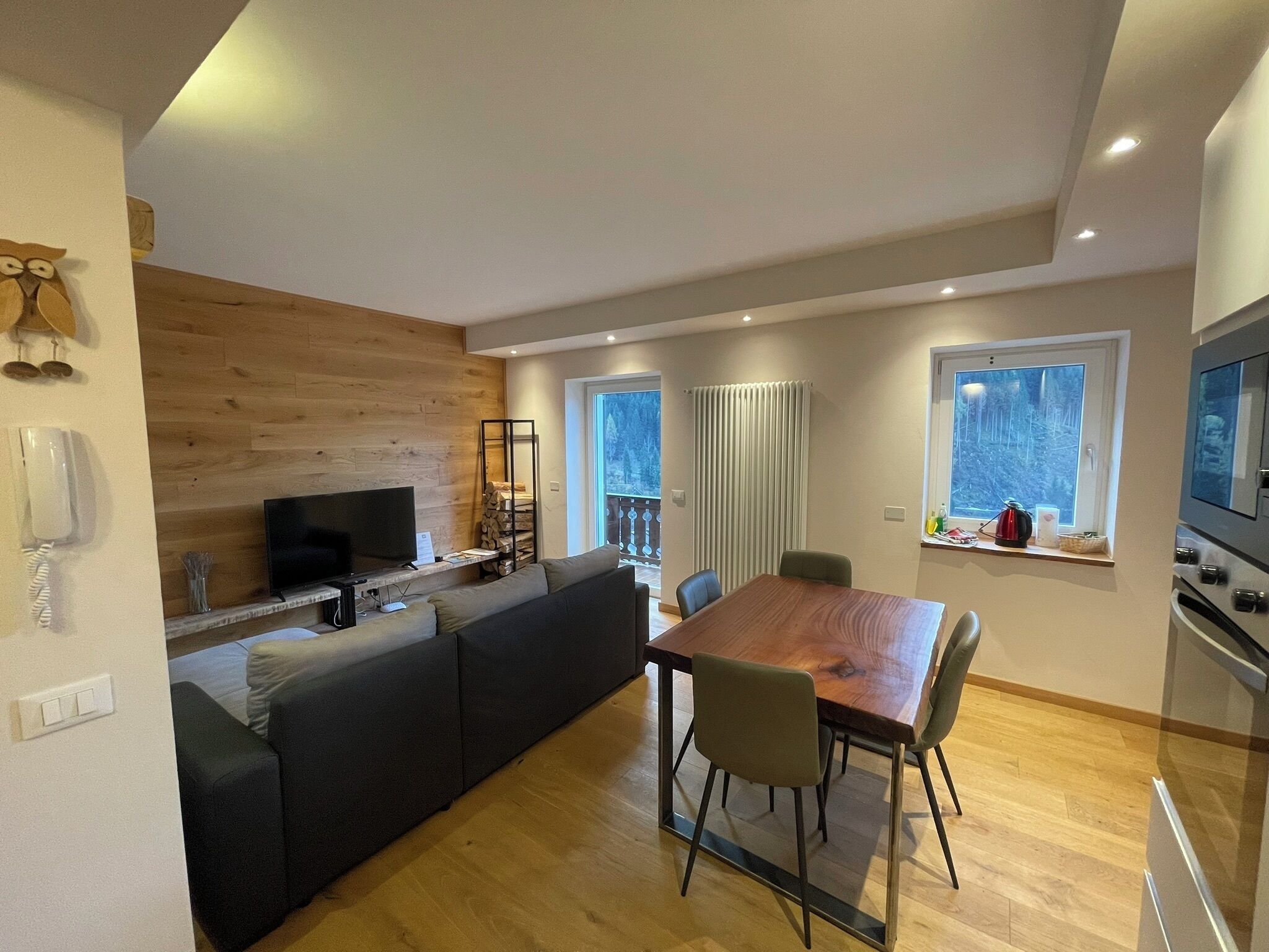 Een moderne woonruimte met een wand van hout, een eethoek met een houten tafel en stoelen, een ingebouwde televisie en een keuken met een fornuis en oven.