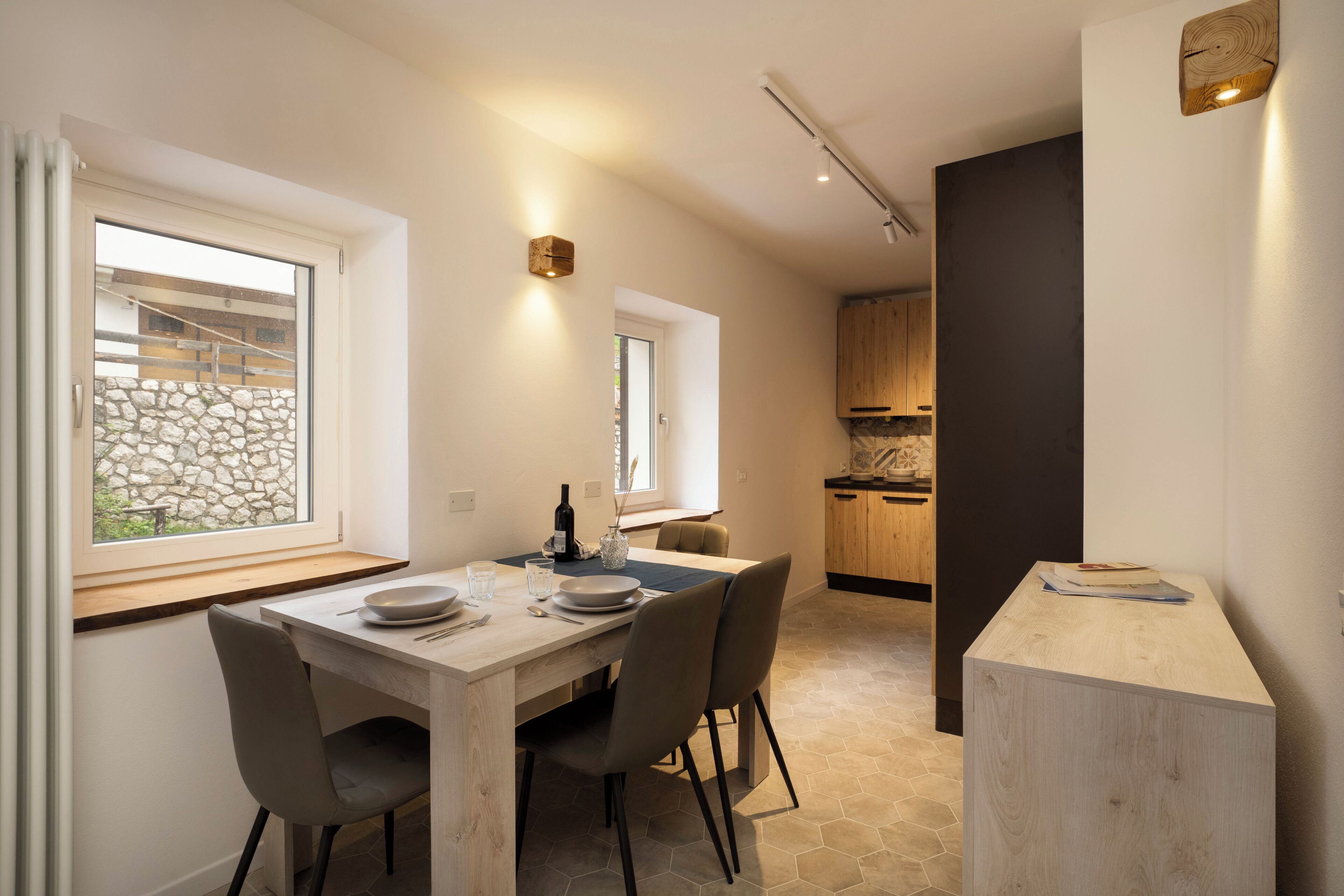 A modern dining area with a wooden table, four chairs, and a window with a stone wall view.