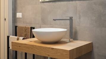 A modern bathroom with a large white vessel sink, a wooden vanity, a black metal stand, and a mirror above the sink.