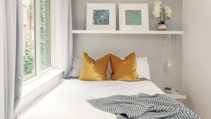 A bedroom with a bed, two gold pillows, a gray and white striped blanket, a nightstand with a small plant, and two framed artworks on the wall. - Spacious 2 bedroom in Liverpool Street (London)