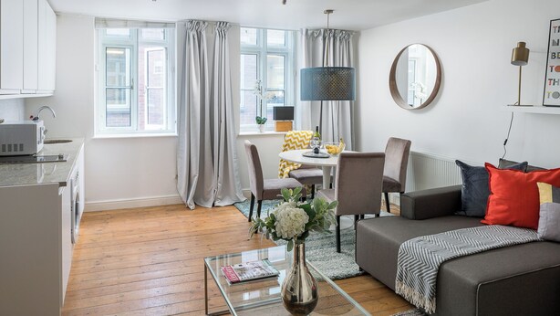 A modern living room with a grey sofa, a glass coffee table, and a dining area with a table and chairs. - Spacious 2 bedroom in Liverpool Street (London)