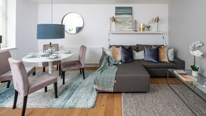 A modern living room with a round dining table, grey sofa, and a blue pendant light. - Spacious 2 bedroom in Liverpool Street (London)