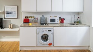 A compact kitchen with white cabinets, a washing machine, a microwave, a toaster, and a sink. - Spacious 2 bedroom in Liverpool Street (London)