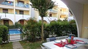 Een patio met een eettafel, omgeven door groen en een zwembad op de achtergrond.