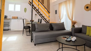 A modern living room with a grey sofa, a round coffee table, and a staircase with wooden railings. - GK Home II part of Gk Fitness Club (Faliraki)