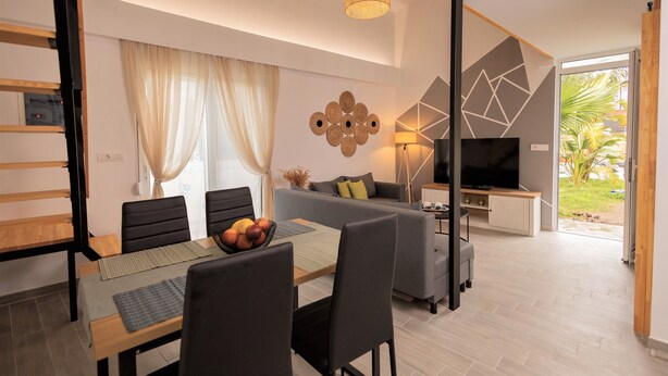 A modern living room with a dining area, a sofa, a TV, and a balcony with a view of greenery. - GK Home II part of Gk Fitness Club (Faliraki)