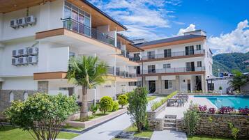 A modern multi-story hotel with balconies, a swimming pool, and landscaped gardens.