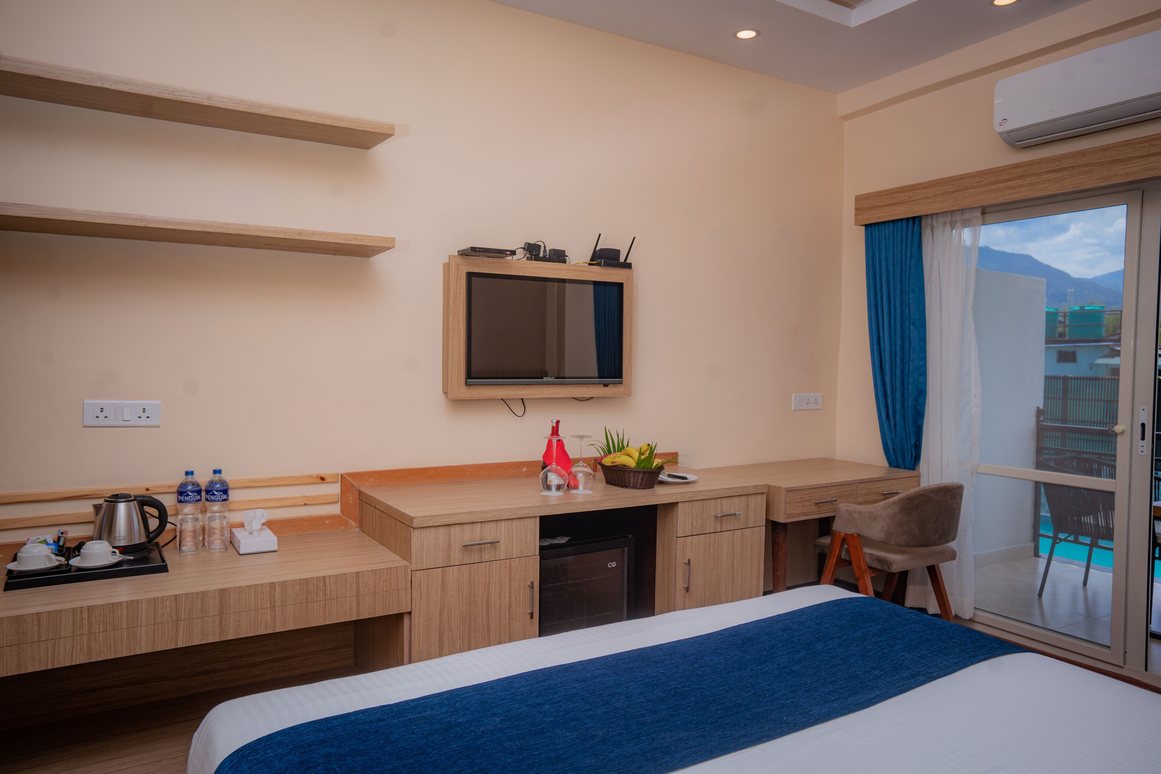 A hotel room with a bed, a desk with a computer, a television, and a window with a view of buildings.
