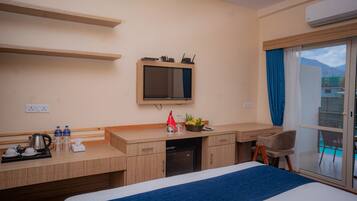A hotel room with a bed, a desk with a computer, a television, and a window with a view of buildings.