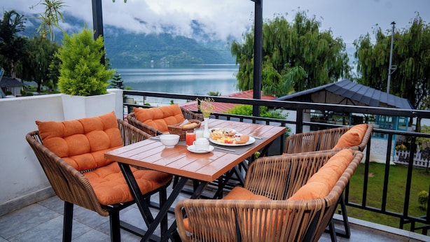 Una terraza con mobiliario de mimbre, una mesa dispuesta con un plato de comida y vistas a un lago y montañas.