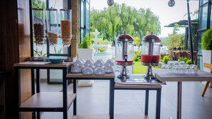 Una cafetería con una máquina de café, un expositor de vidrio con bocadillos y vistas a un jardín a través de grandes ventanales.