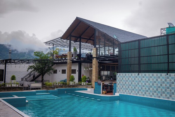 A swimming pool area with a covered seating area and a view of a mountain. - Majestic Lakefront Hotel & Suites (Pokhara)
