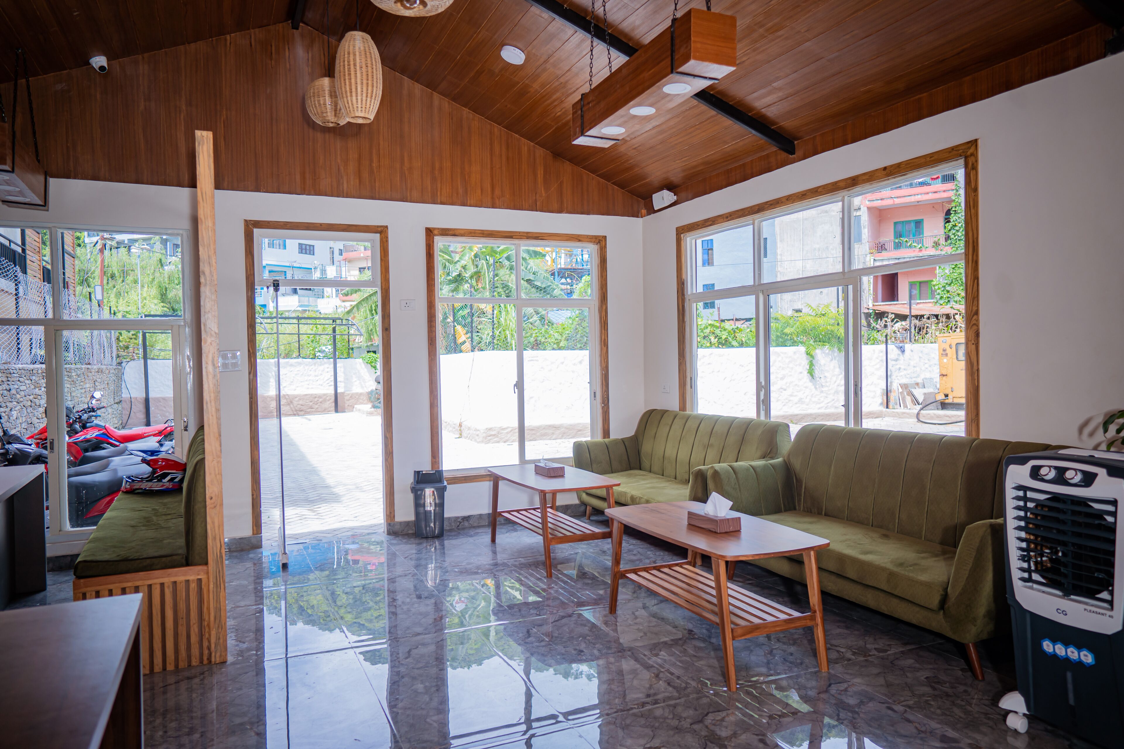 A spacious room with a wooden ceiling, large windows, a green sofa, a wooden table, and a ceiling fan.