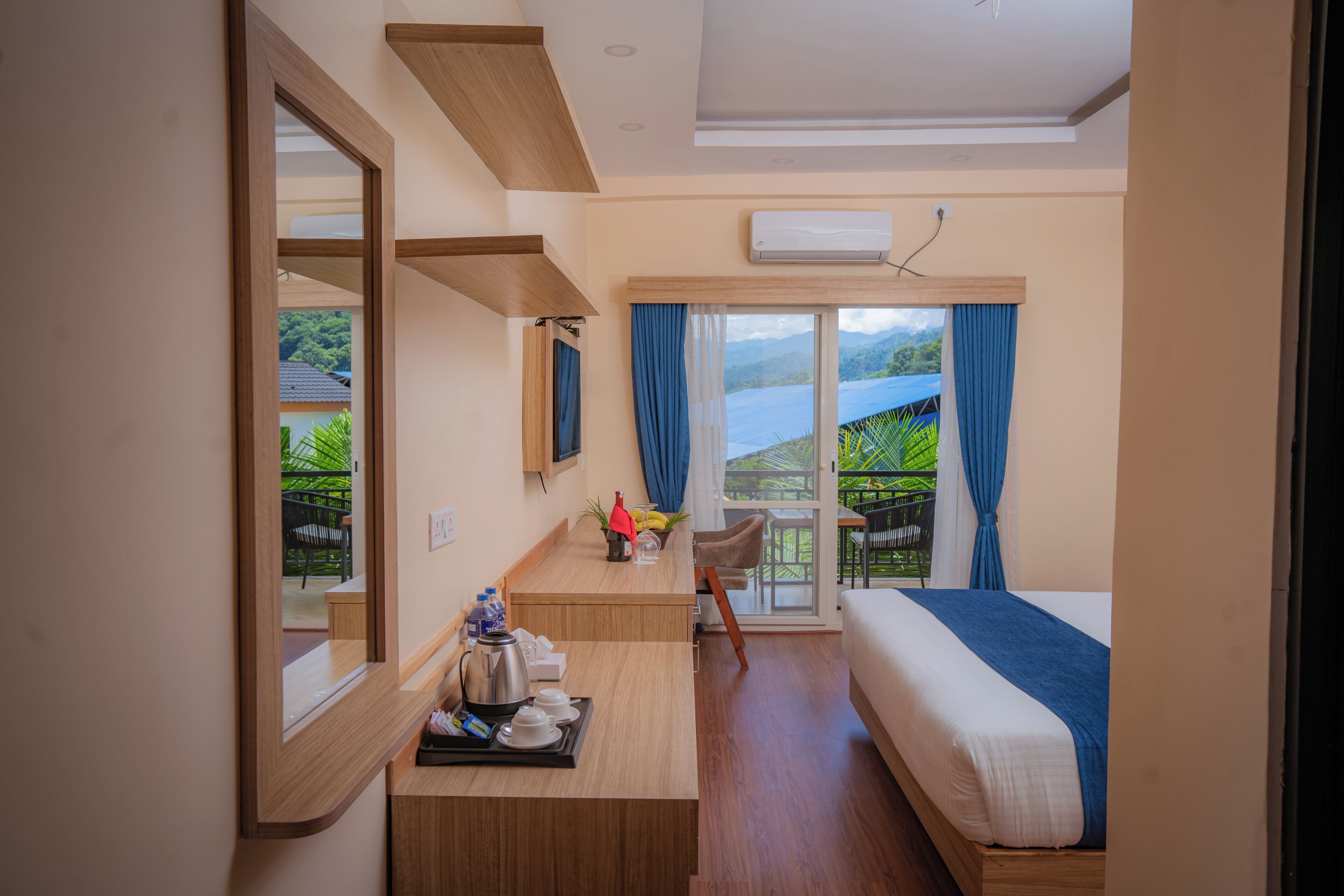 A hotel room with a bed, a desk with a tray of breakfast items, a chair, and a view of a green landscape through the window.