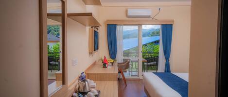 A hotel room with a bed, a desk with a tray of breakfast items, a chair, and a view of a green landscape through the window.