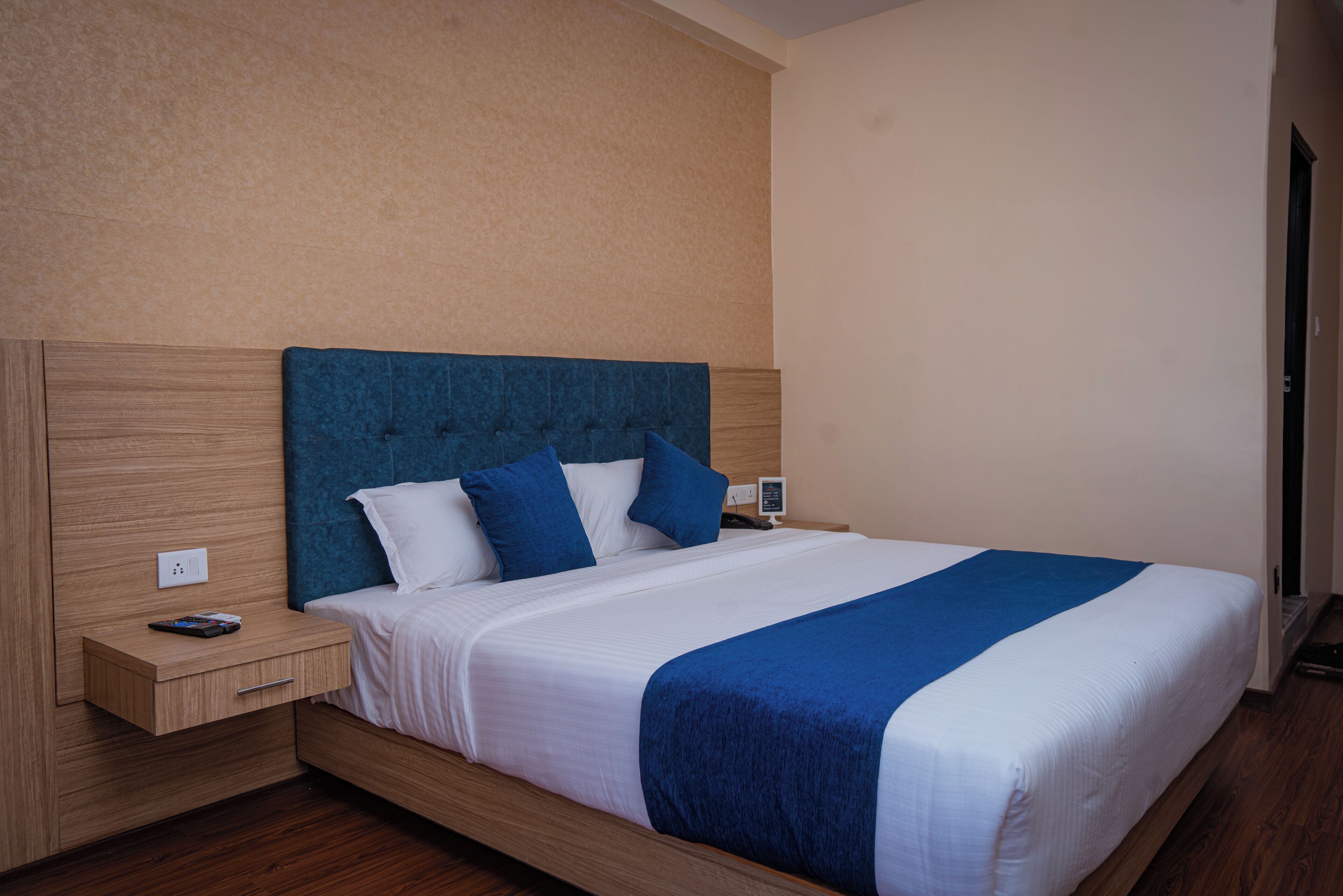 Un lit bien fait, avec une tête de lit bleue, du linge de lit blanc et un élément décoratif bleu. On y trouve une table de chevet en bois sur laquelle sont posés un téléphone et une télécommande.