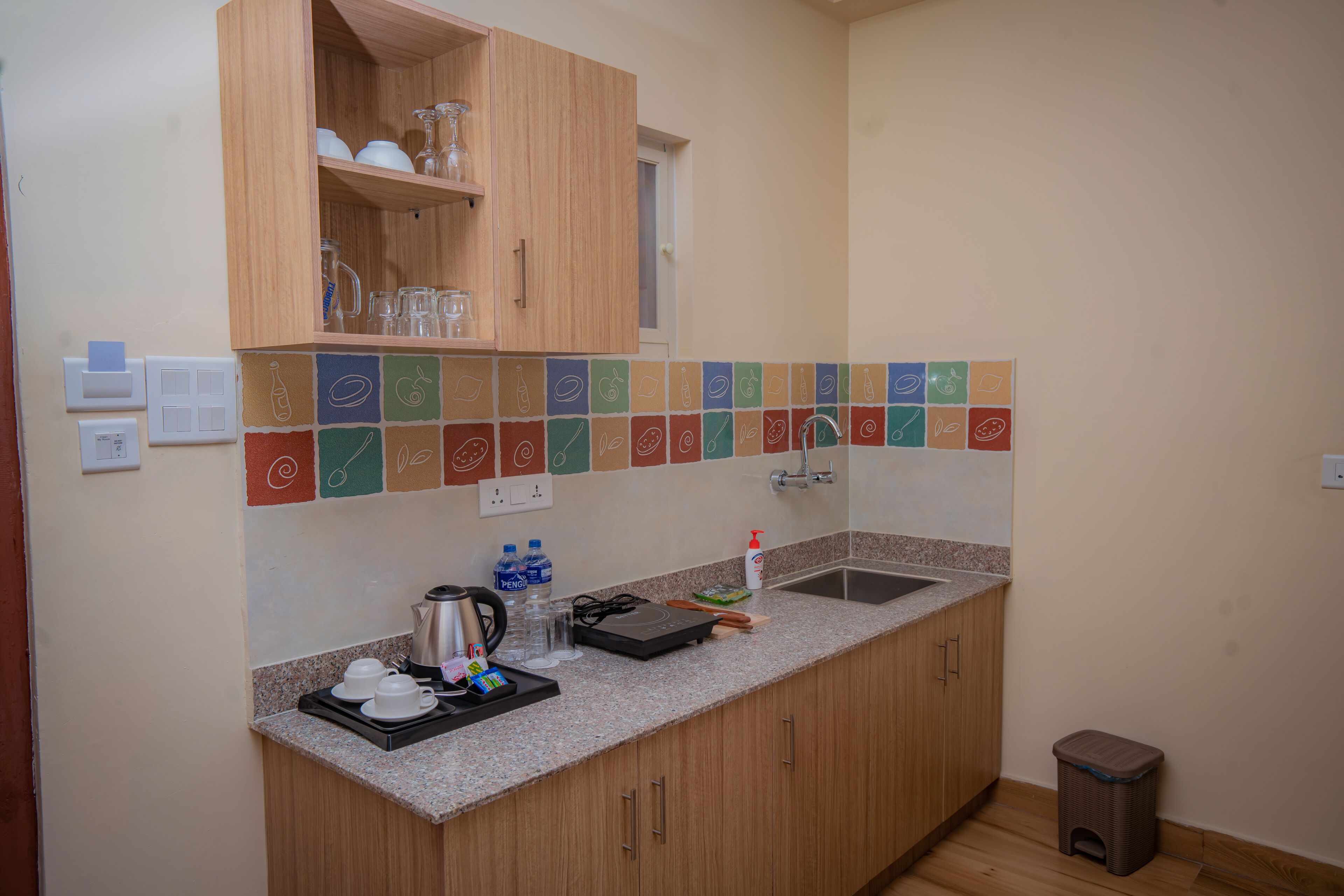 A kitchen with wooden cabinets, a granite countertop, a sink, and a tiled backsplash with food illustrations.