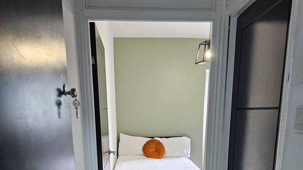 A narrow hallway leading to a bedroom with a bed, a door, and a light fixture. - Skyline King Studio Room 201 (Swansea)