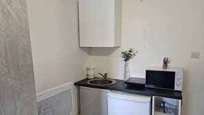 A compact kitchenette with a sink, a microwave, and a small cabinet. - Skyline King Studio Room 201 (Swansea)