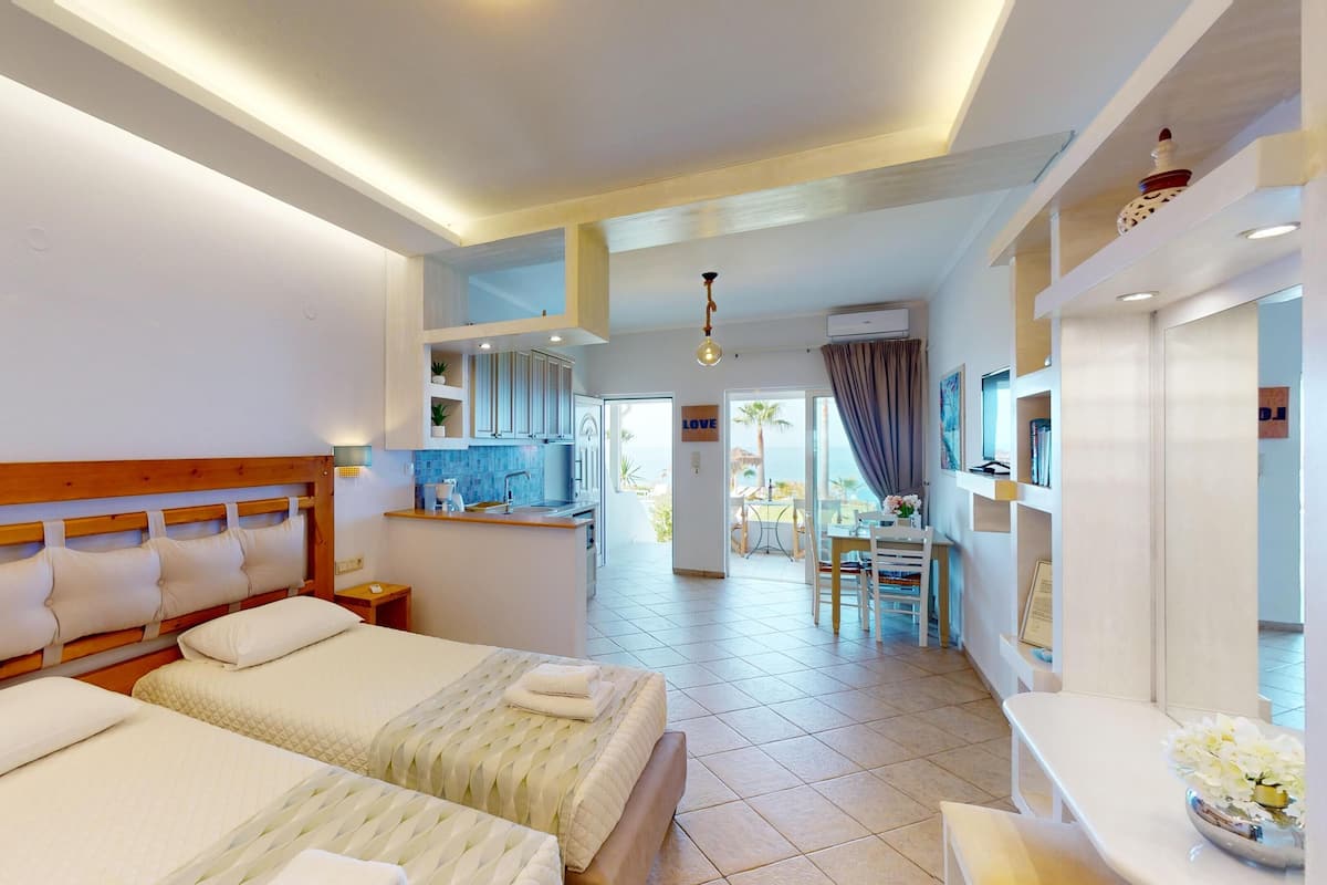 A hotel room with two beds, a kitchenette, a dining area, and a view of the sea.