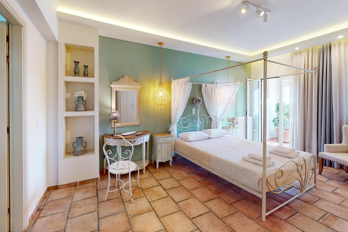 A bedroom with a four-poster bed, a bedside table, a small chair, a shelf with decorative items, and a window with curtains.