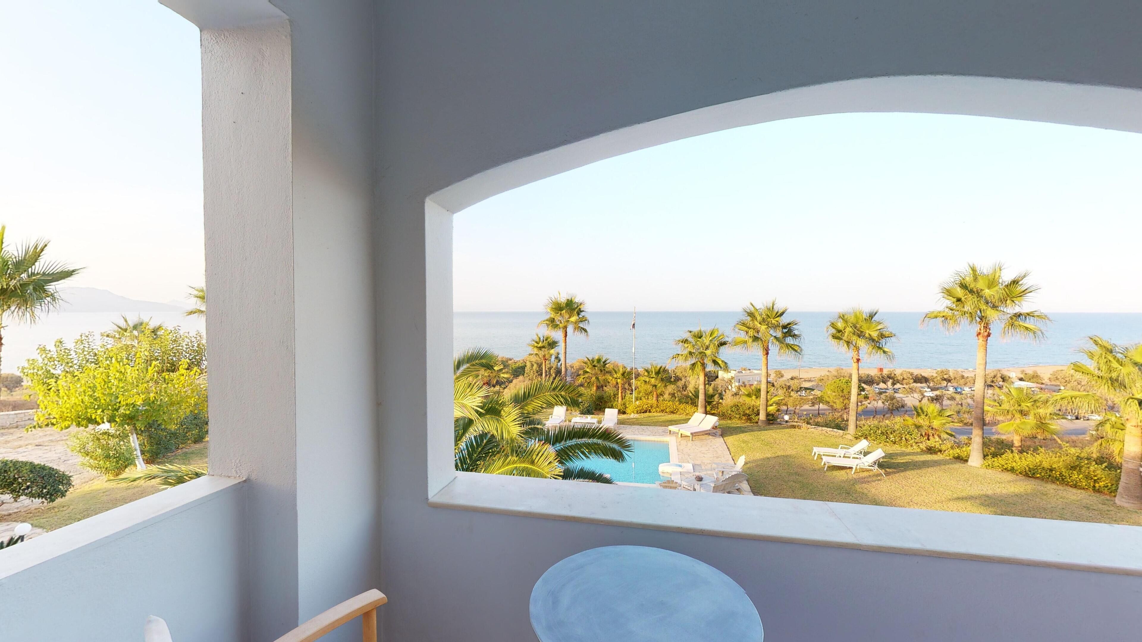 Ein Balkon mit Blick auf einen Pool, Palmen und das Meer.