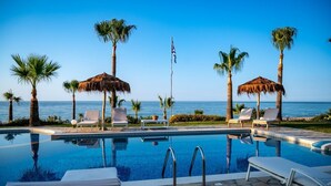 A pool area with lounge chairs and umbrellas, overlooking a body of water. - Aneria Suites (Rethymno)