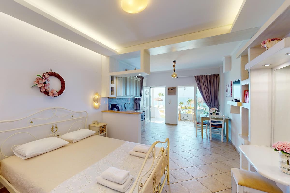 A bedroom with a bed, bedside table, and a view of the kitchen and balcony.