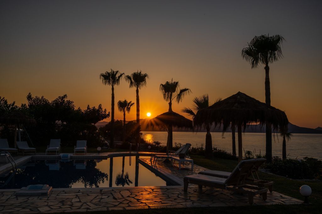 Zonsondergang boven een zwembad met ligbedden en palmbomen.