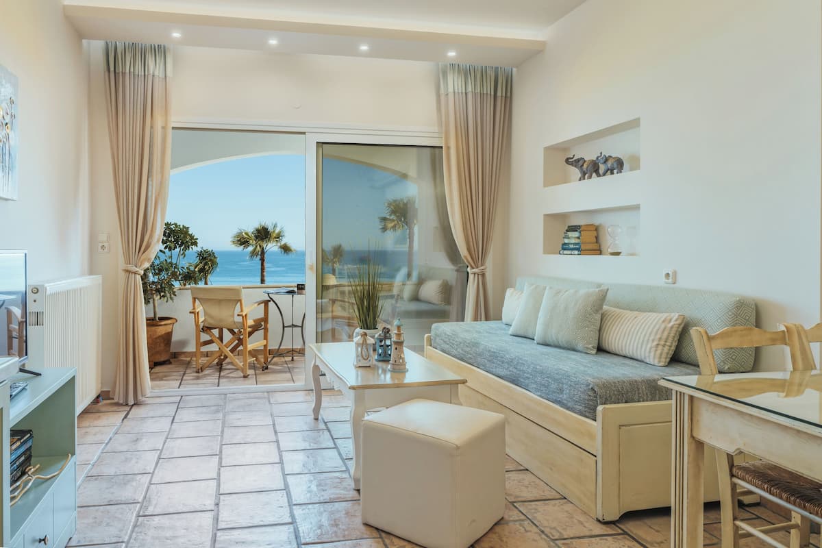 A living room with a sofa, a coffee table, and a dining table. There is a view of the ocean through large windows.